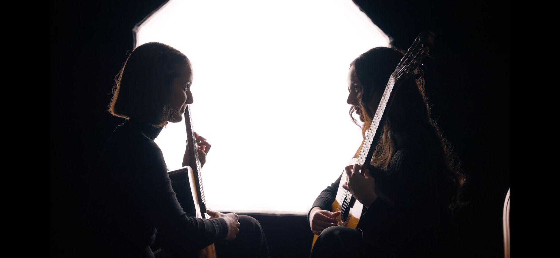 Silhouettes of the two guitarists facing each other against bright studio light