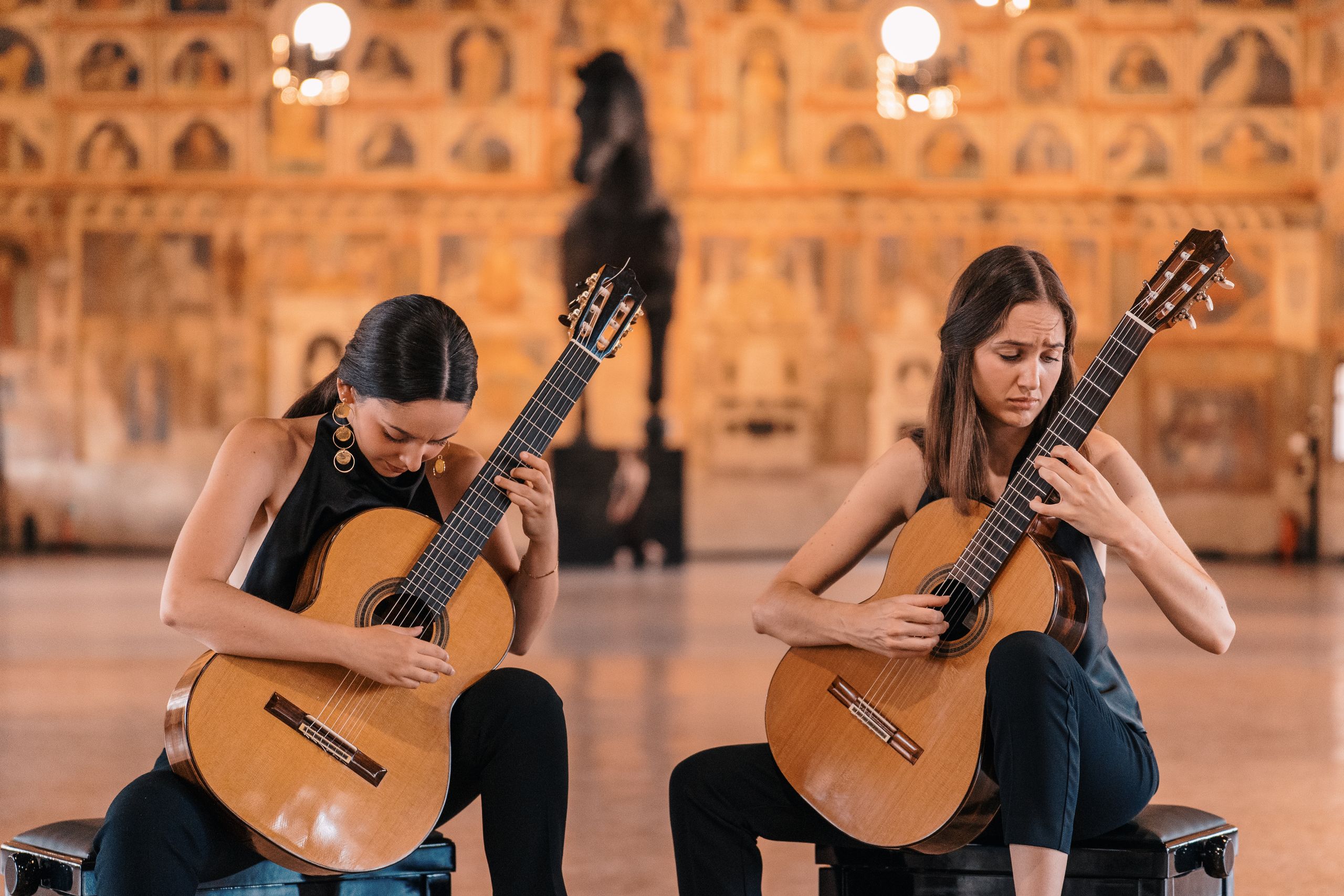 Alice Brandão and Maja Kralj of the Daniyah Guitar Duo performing on classical guitars in a grand frescoed hall